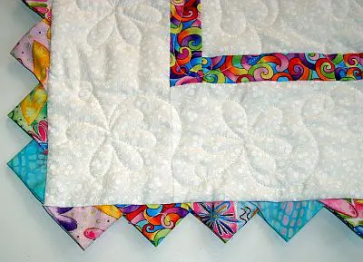 Colorful handmade quilt with scalloped borders and binding, featuring a white center with quilted floral pattern. - Looney Bin Quilting