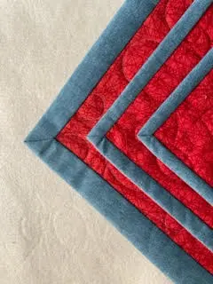 Handmade quilt with red and blue fabric layers, featuring double binding detail. - Looney Bin Quilting