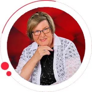 Portrait of a smiling woman with glasses wearing a white lace shirt. - Looney Bin Quilting